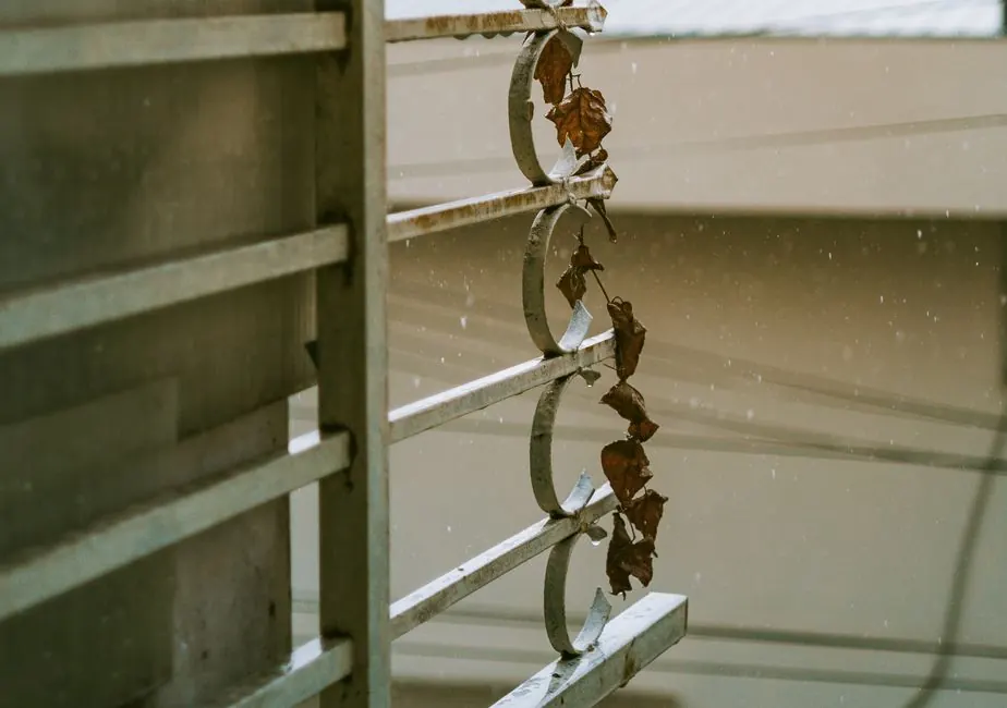 A close-up of a rustic metal grill adorned with dry leaves during a rainy day, capturing a moody atmosphere.