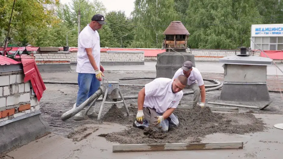 Team of construction workers laying concrete on a rooftop, emphasizing teamwork.